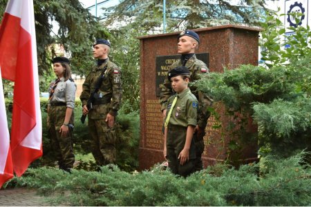 Warta honorowa przy pamiątkowej tablicy poświęconej ciechanowianom walczącym w Powstaniu Warszawskim. Po obu stronach marmurowego monumentu z pamiątkową płytą stoi dwóch dorosłych mundurowych i dwoje małych harcerzy.