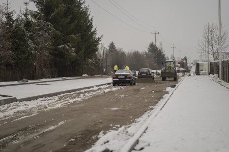 Ulica Opinogórska. Zdjęcie zrobione po opadach śniegu. Chodniki po obu stronach jezdni są pokryte białym puchem. Na gruntowej jezdni nie ma śniegu. W oddali stoją dwa osobowe auta, a dalej sprzęt budowlany: spychacz i duża koparka. Po lewej stronie drogi rosną duże drzewa.