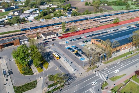 Zdjęcie wykonane z lotu ptaka. Uchwycono otoczenie dworca kolejowego (po lewej) i hali targowej (po prawej) oraz miejsca parkingowe w ich sąsiedztwie. Od góry zdjęcie zamykają tory kolejowe, a od dołu ulica Sienkiewicza.