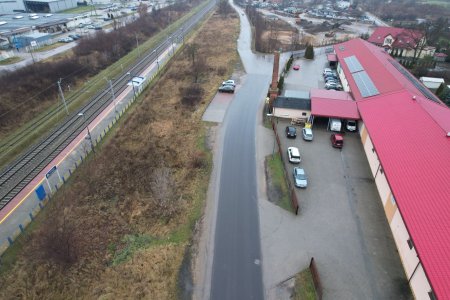 Zdjęcie wykonane z góry. Po lewej są tory kolejowe. Po prawej stronie, wzdłuż torów biegnie długi, szeroki zachwaszczony pas ziemi. Środkiem zdjęcia biegnie wąska ulica Fabryczna. Po prawej znajduje się długi budynek pokryty czerwonym dachem, należący do Hurtowni Sigma-Max. U góry, za budynkiem zaczyna się ulica Augustiańska. Idzie łukiem w prawo i dalej prosto.