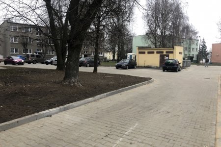 Nowa droga z brukowej kostki. Po lewej trawnik, a w głębi parking i budynek z trzema kondygnacjami.