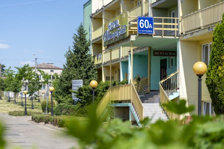 Hotel Olimpijski w Ciechanowie. Oddany do użytku 30 lat temu. Ma żółte ściany zewnętrzne. Pokoje od tej strony budynku wyposażone są w balkony w betonowych wnękach. Przed hotelem rosną średnie i niskie drzewka. Jest tu też niski żywopłot wokół małego trawnika.