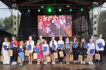 Grupa dzieci z prezydentem Krzysztofem Kosińskim pozuje do pamiątkowej fotografii. Stoją na scenie rozstawionej na zamkowych błoniach. Każdy z nagrodzonych trzyma w rękach niebieską teczkę z listem gratulacyjnym od prezydenta Ciechanowa.