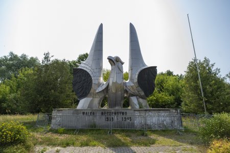 Pomnik Walka Męczeństwo Zwycięstwo 1939-1945. Na szerokim postumencie znajduje się popiersie orła z dumnie uniesionym dziobem i głową skierowaną w lewo (w lewo patrzącego na zdjęcie). Skrzydła orła przypominają skrzydła samolotu, ale nie są poziomo rozłożone na boki. Sterczą pionowo, sięgając wysoko ponad głowę orła. Poniżej po obu stronach znajdują się ciemne płaskorzeźby, przedstawiające żołnierzy. Pomnik jest otoczony barierkami. Po prawej stoi maszt, na który podczas świąt narodowych wciągana jest flag. Pomnik stoi na tle bujnej zieleni zespołu przyrodniczo-krajobrazowego Dolina Rzeki Łydyni.