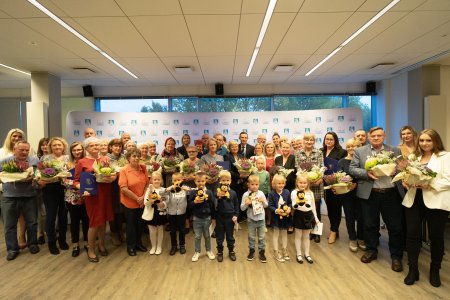 Wielu uczestników konkursu na najładniejszą posesję na pamiątkowej fotografii z prezydentem Krzysztofem Kosińskim. Każdy z uczestników ma w rękach bukiet kwiatów i dyplom. W pierwszym rzędzie stoją odświętnie ubrane dzieci w wieku przedszkolnym, które trzymają w rękach pszczółki-maskotki oraz dyplomy.