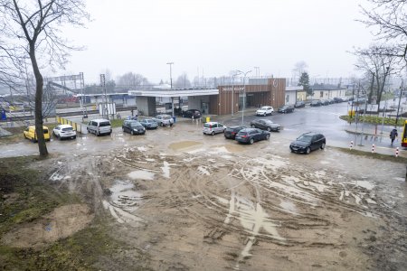 Fragment placu, na którym powstanie nowy parking. W pobliżu znajduje się budynek dworca kolejowego, a przy nim zaparkowane auta. Po prawej znalazł się także fragment przydworcowego skweru.