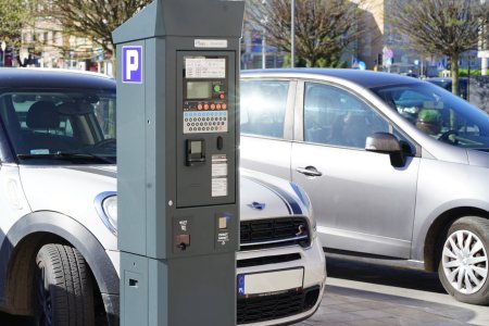 Parkometr, w ktorym wprowadzono możliwość płacenia za parking zbliżeniowo, przy pomocy karty. Obok parkometru stoją dwa samochody osobowe.