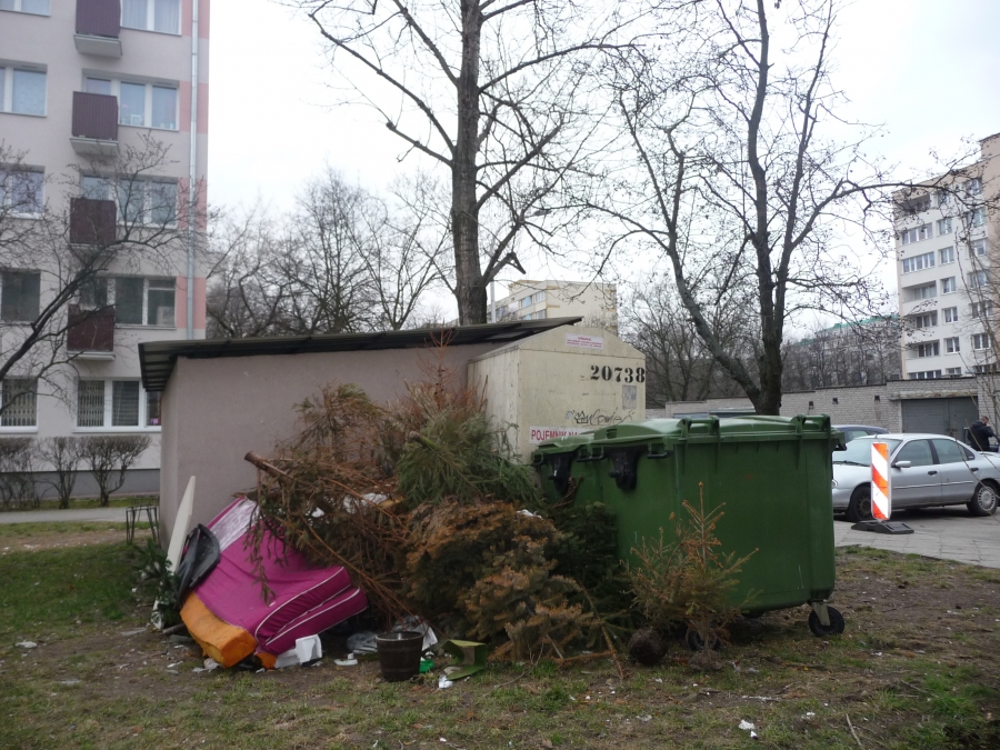 Przy murowanym śmietniku na osiedlu domów wielorodzinnych usypana góra śmieci i suchych gałęzi